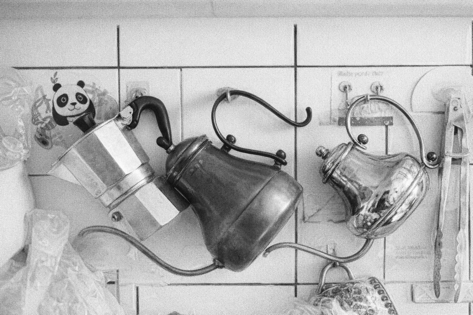 Mustavalkoinen kuva seinällä riippuvista keittiövälineistä ja pannuista.