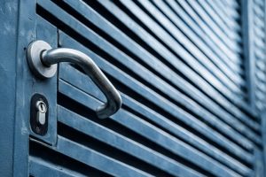 Lähikuva metallisesta ovenkahvasta ja lukosta sinisessä säleovessa.